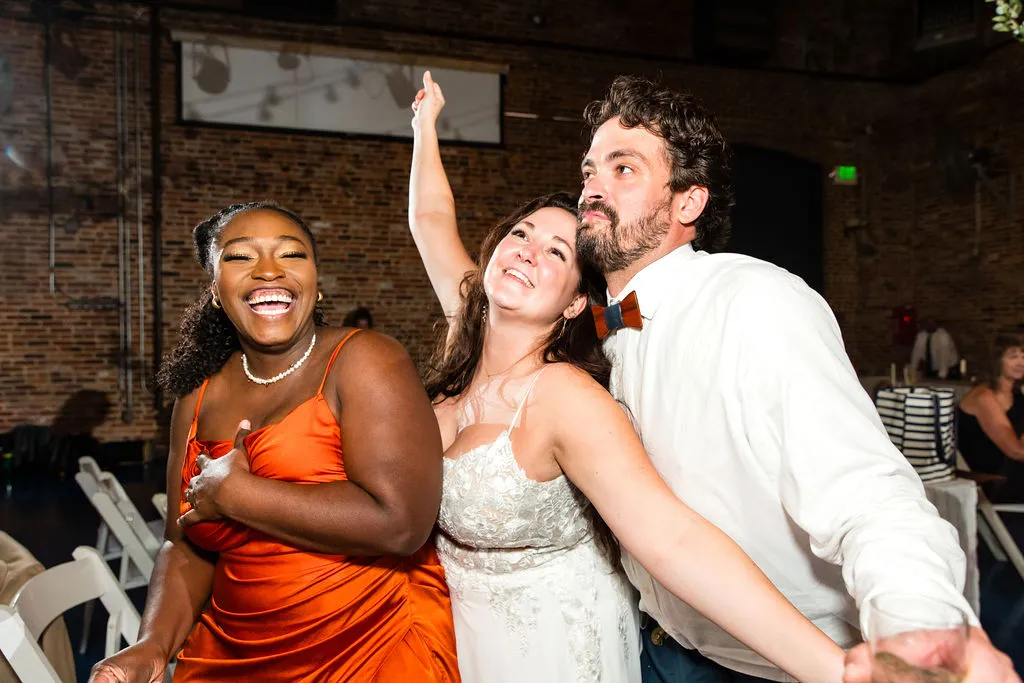 bride, groom, and woman in orange dress dancing close