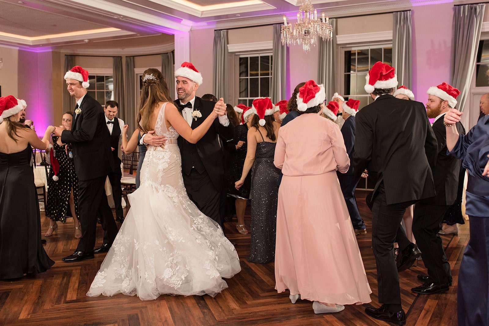 bride and groom dance with guests while all wearing Santa hats