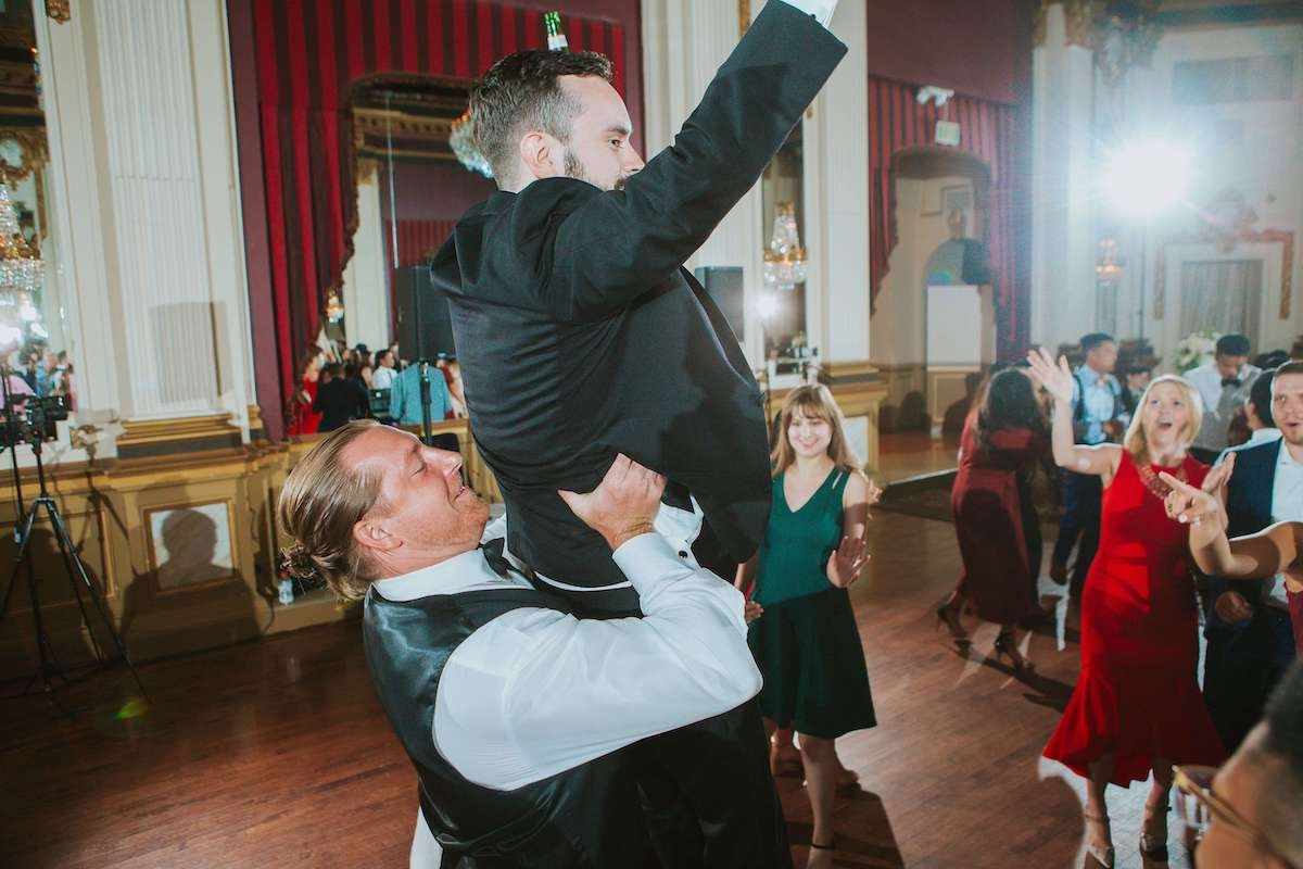 guy lifts up groomsman at wedding on dance floor