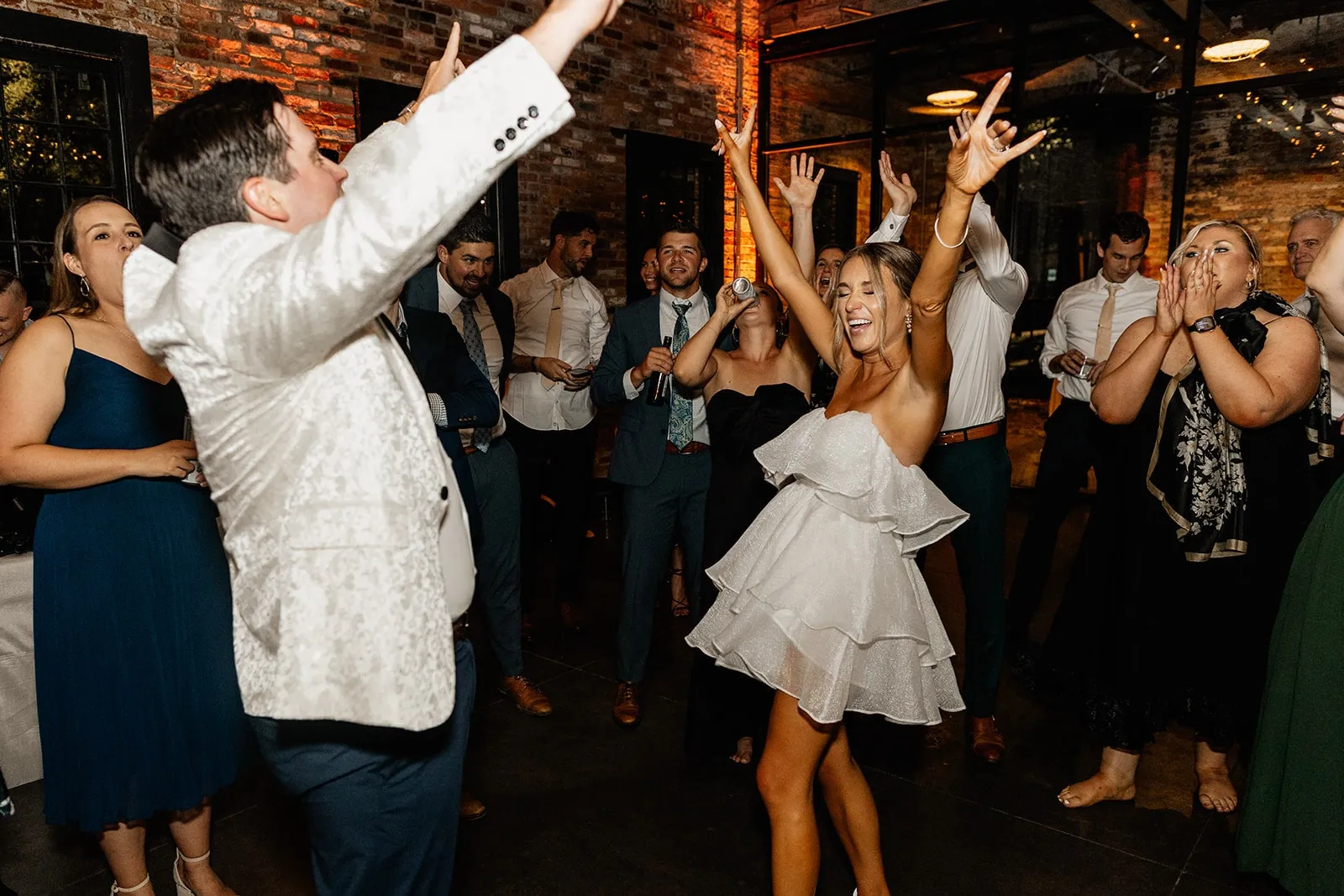 bride and groom dancing with hands up surrounded by friends