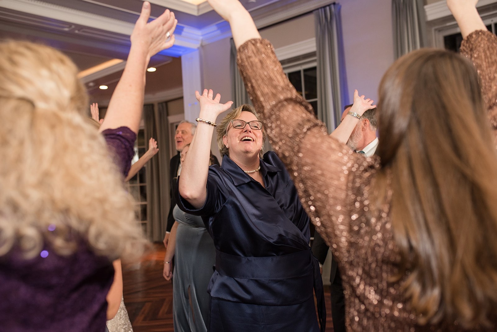 older woman in navy-colored dress dancing with hands up at wedding