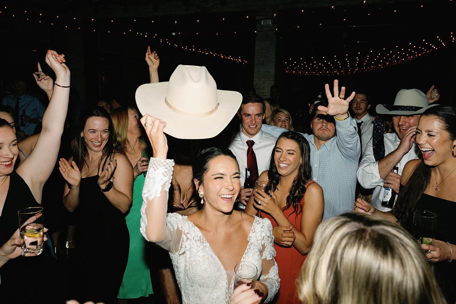 bride smiling and lifting up cowboy hat while guests clap