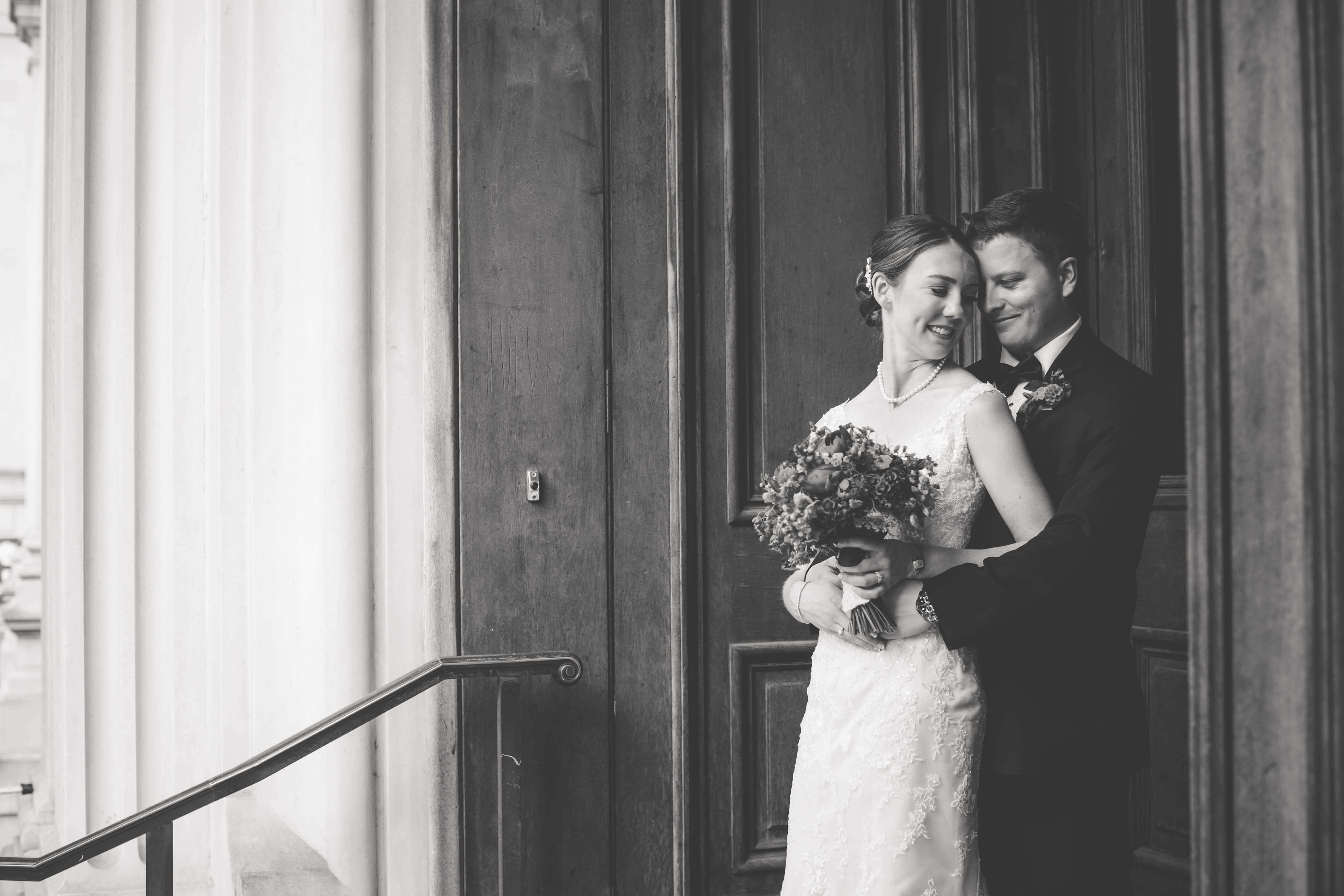 bride and groom pose by old door and railing