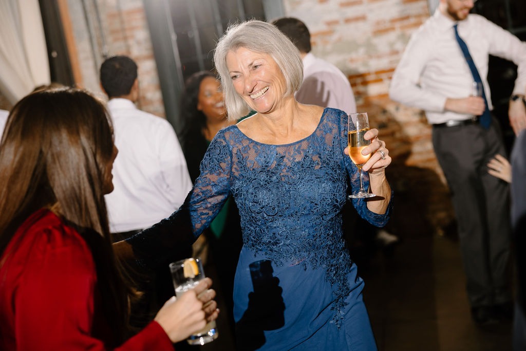 older woman in blue dress dancing at wedding with a glass of white wine in hand