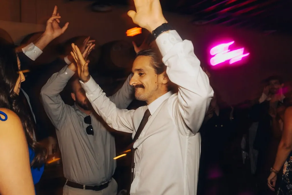 young guy with mustache dancing at wedding with hands up