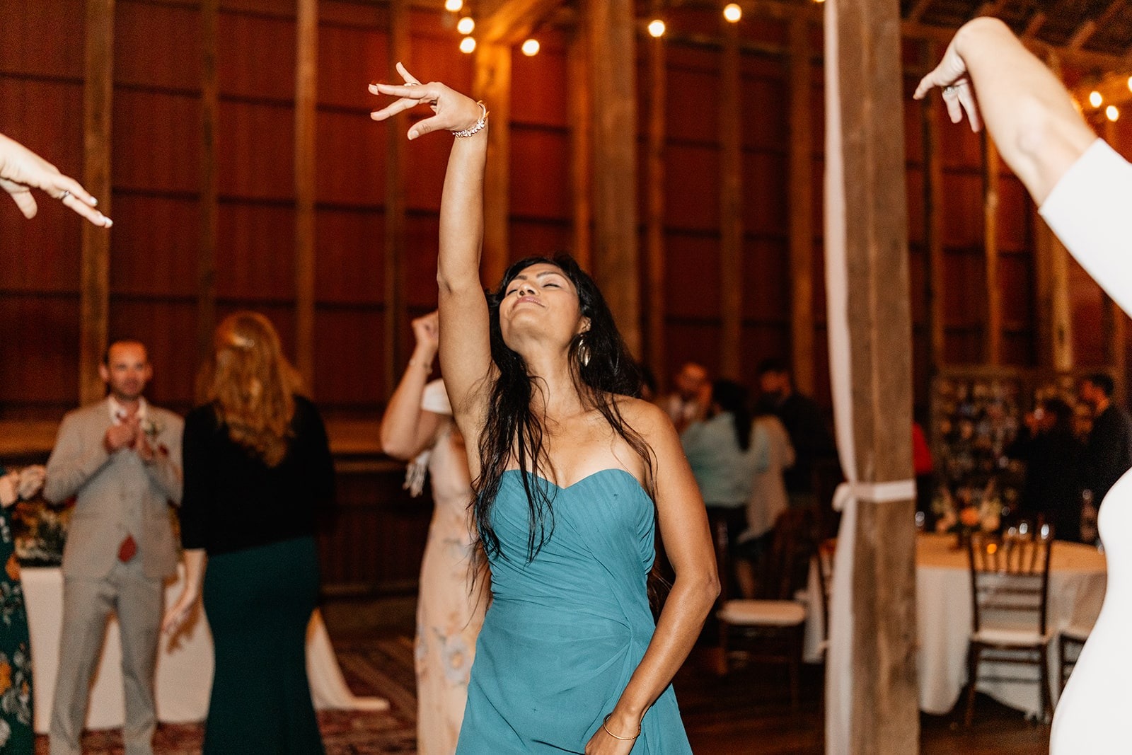 woman in teal dress dancing at wedding with hand up