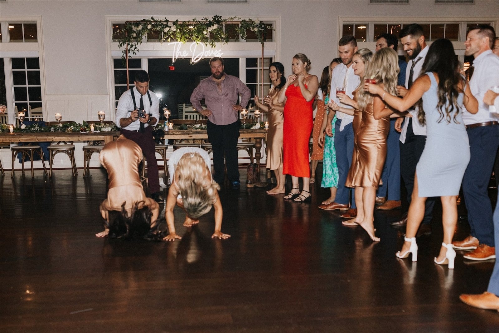 bridesmaid and bride doing a somersault on wedding dance floor while guests on the right watch