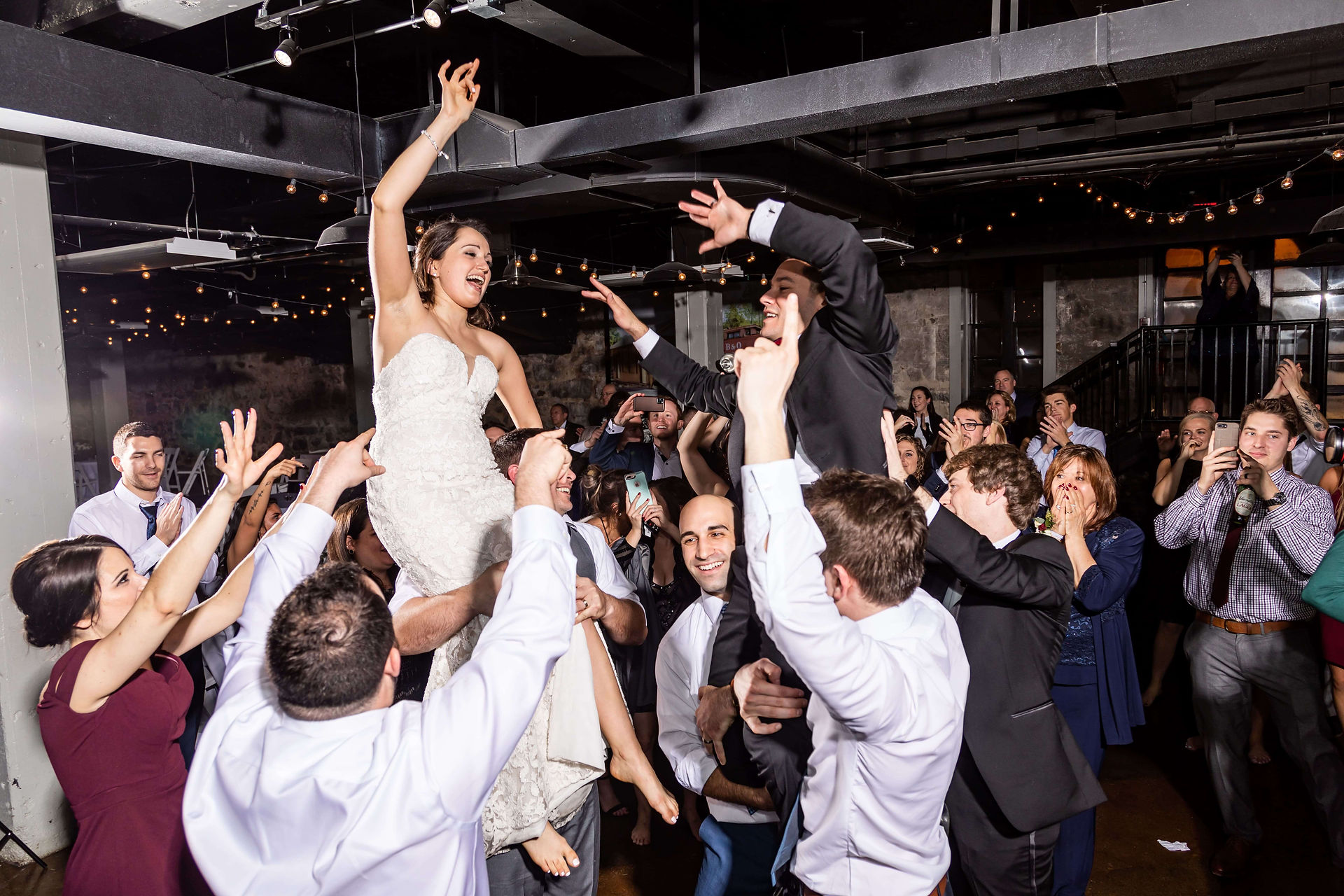 wedding guests hold up bride and groom on their shoulders