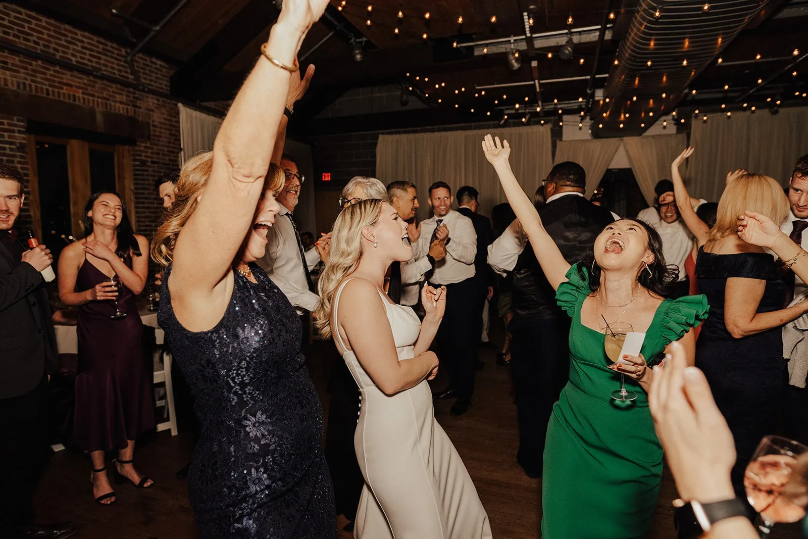 bride and woman in green dress dancing at wedding with guests