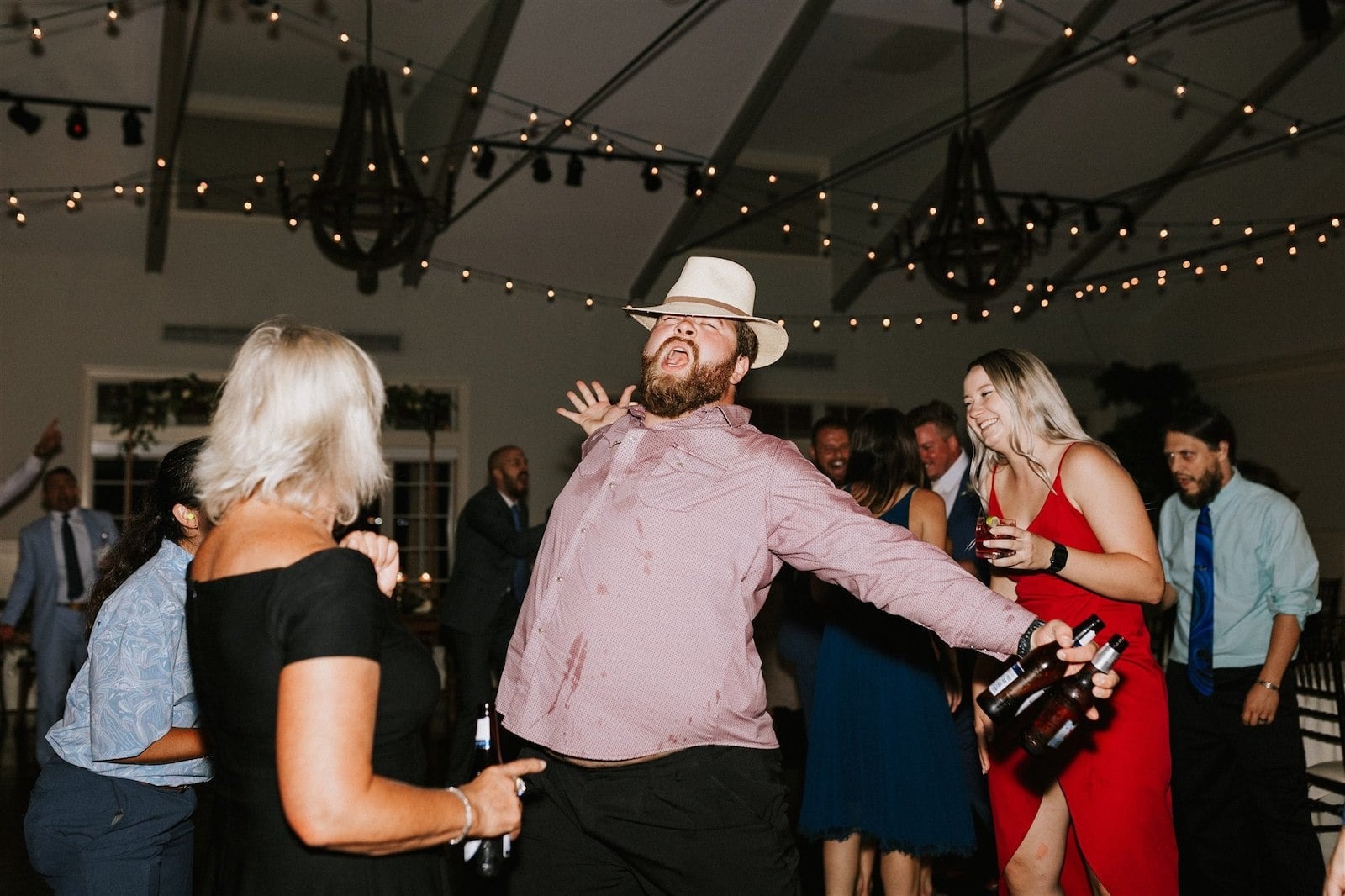 guy in pink shirt and hat dancing with two beers in hand