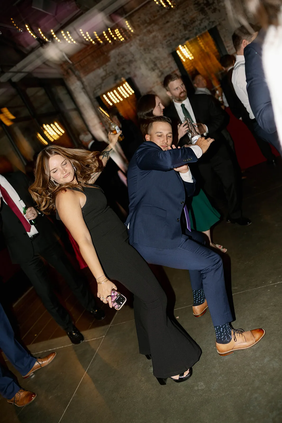 woman in black dress dancing behind man in navy suit at wedding