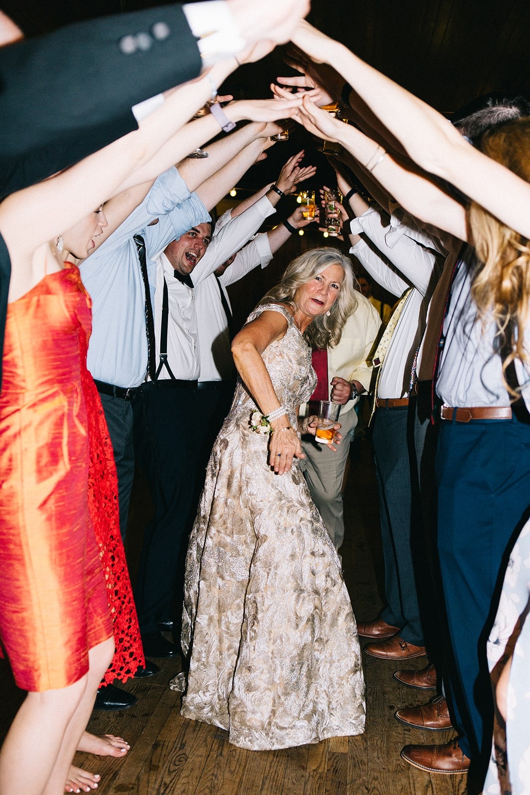 older woman in long formal dress down tunnel of people at wedding