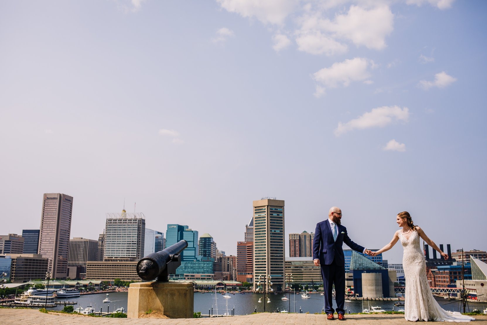 bride and groom pose next to cannon with city scape in the background