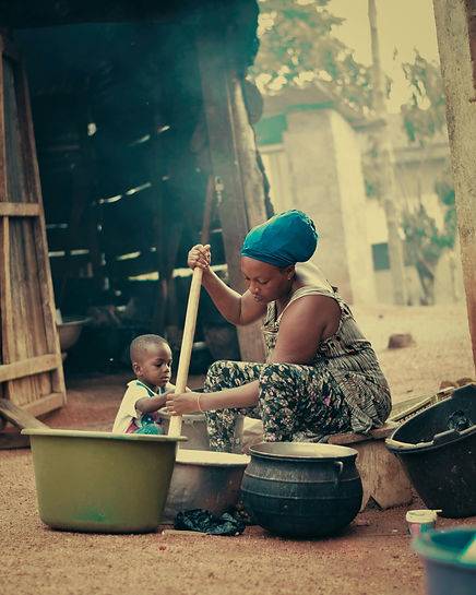 African woman making food with her child next to her