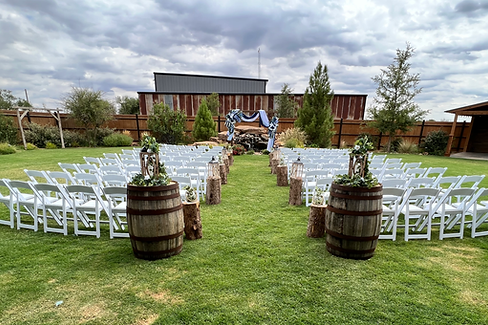 Wedding ceremony setup with white chairs, wooden barrels, and green grass field