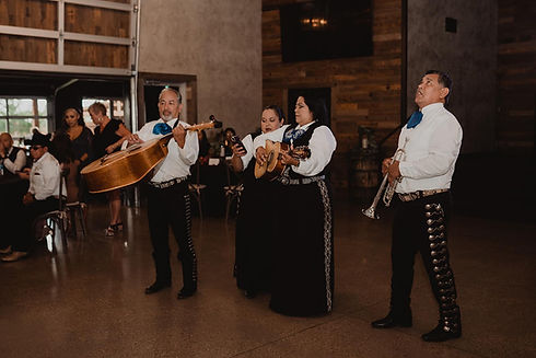 Mariachi band playing instruments inside a venue with people in the background.