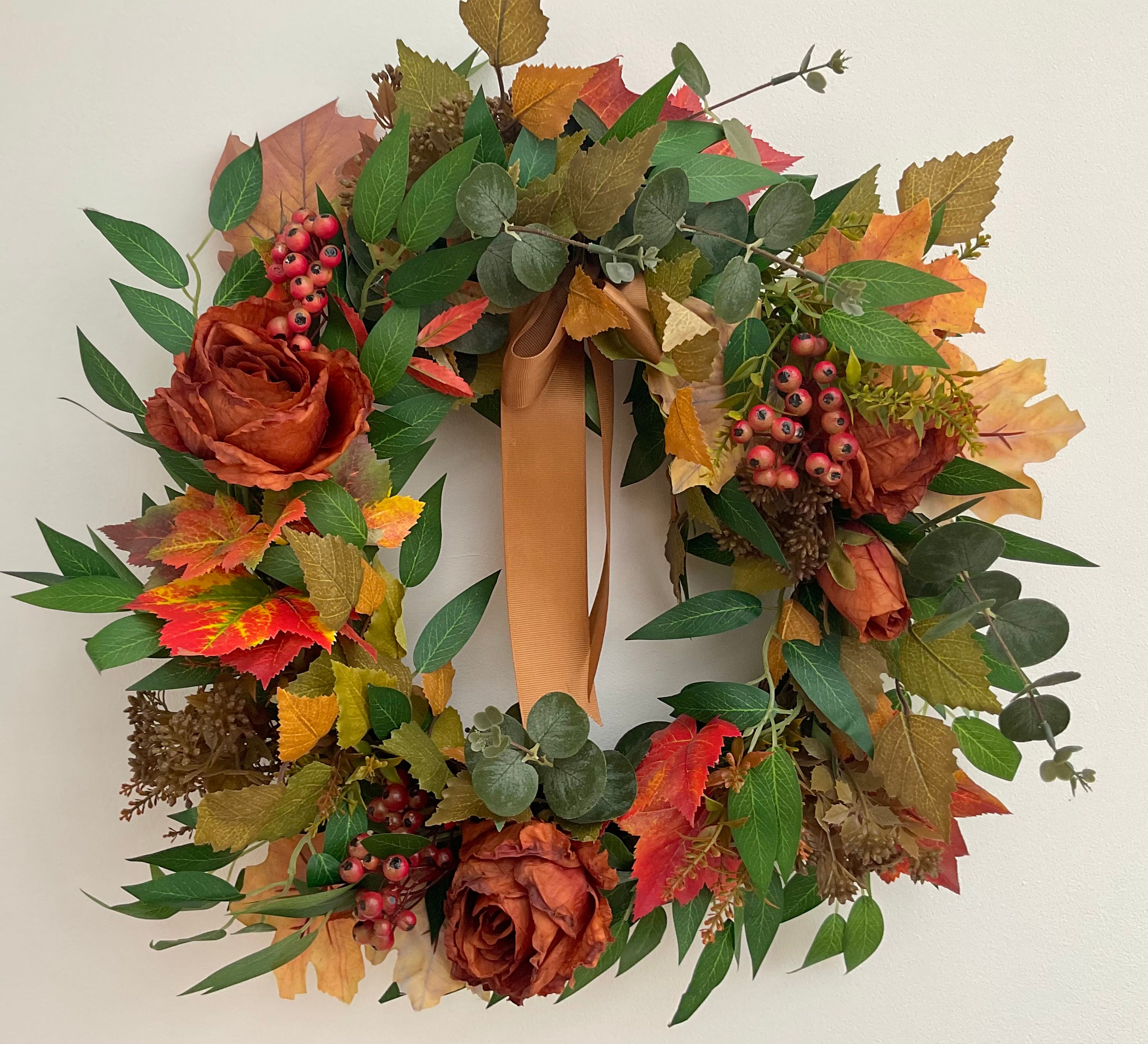 Full Rust Rose Ember Autumn wreath with faux roses, berries, rust foliage, and pale caramel velvet bow on grapevine frame.