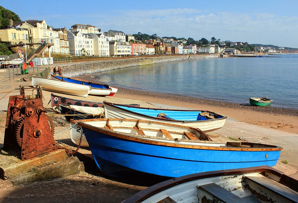 A photograph of Dawlish, Devon County, England. Small boats line the cozy shoreline. Credit to Devon Guide.