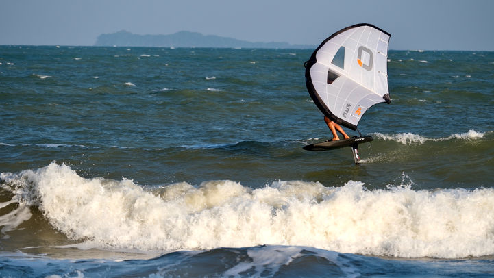 Wing foiler riding waves close to shore with Thai island visible on horizon in background