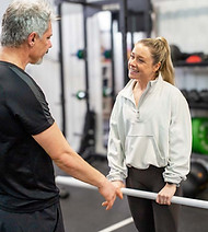 Female PT talking to a male weight loss client in a gym.