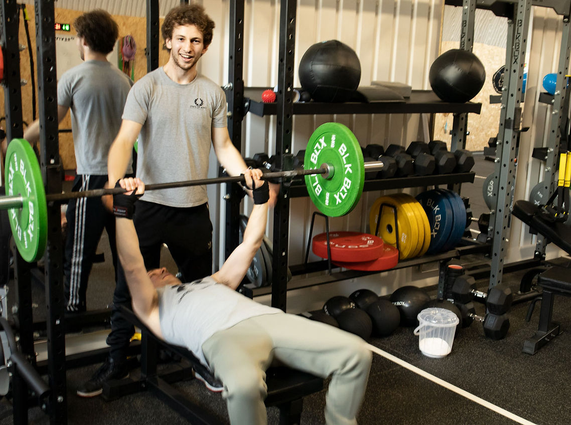 Ealing personal trainer training studio smiling and helping a male client with the bench press.
