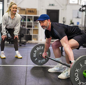 Personal trainer watching on as a middle aged client braces before a deadlift.