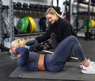 Personal trainer guiding a female client through a crunching ab exercise.