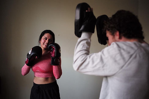 Personal boxing trainer holding pads for female client who is smiling.