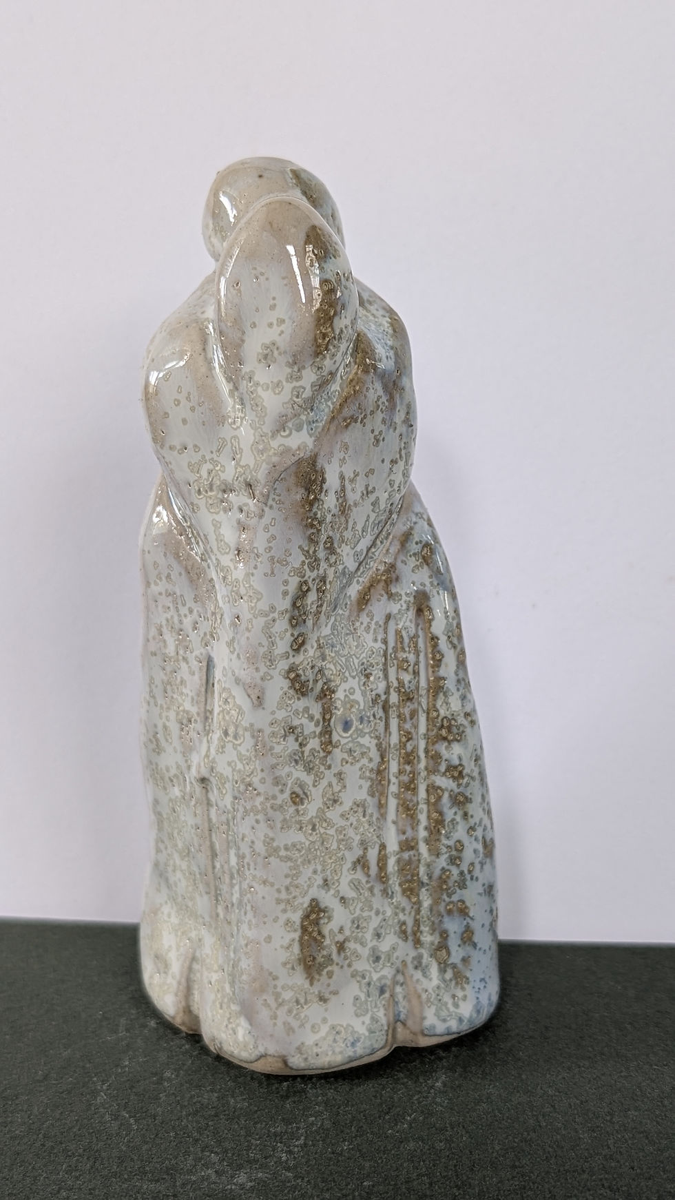 cream colored and textured ceramic sculpture of two people intertwined in a hug making them appear like one person
