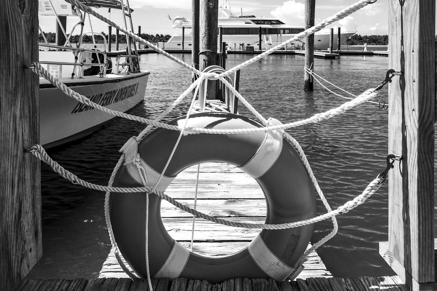 Lifesaving ring on Beaufort boardwalk dock with boats in the distance on calm water, evoking nautical charm.