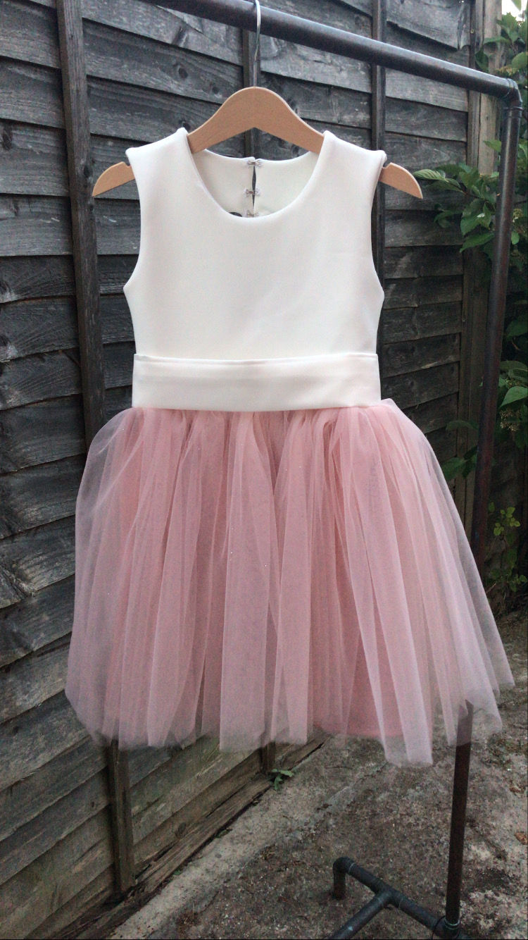 Thumbnail: A handmade ivory white and blush pink tutu dress with a heart cut out back. It features a soft blush tulle skirt that falls knee length and a large duchess satin bow sash. The perfect flower girl, birthday dress or Christmas party dress