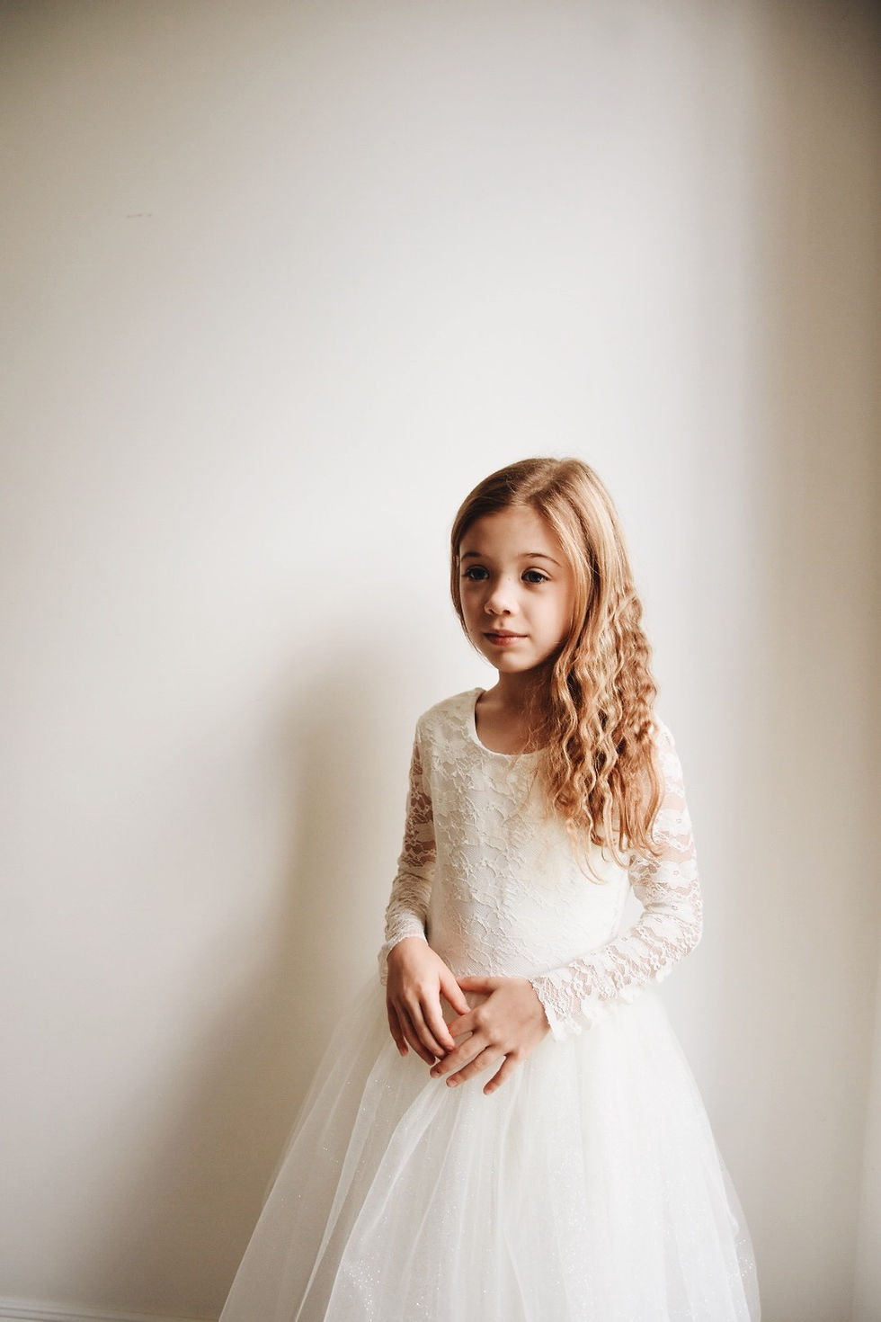 Thumbnail: A handmade ivory white lace tutu dress which features long lace sheer sleeves and a V pearl button back. The sparkly tutu skirt falls to the floor and has a large duchess satin bow sash around the waist. The perfect flower girl, birthday dress or Christmas party dress. Perfect Holy Communion dress