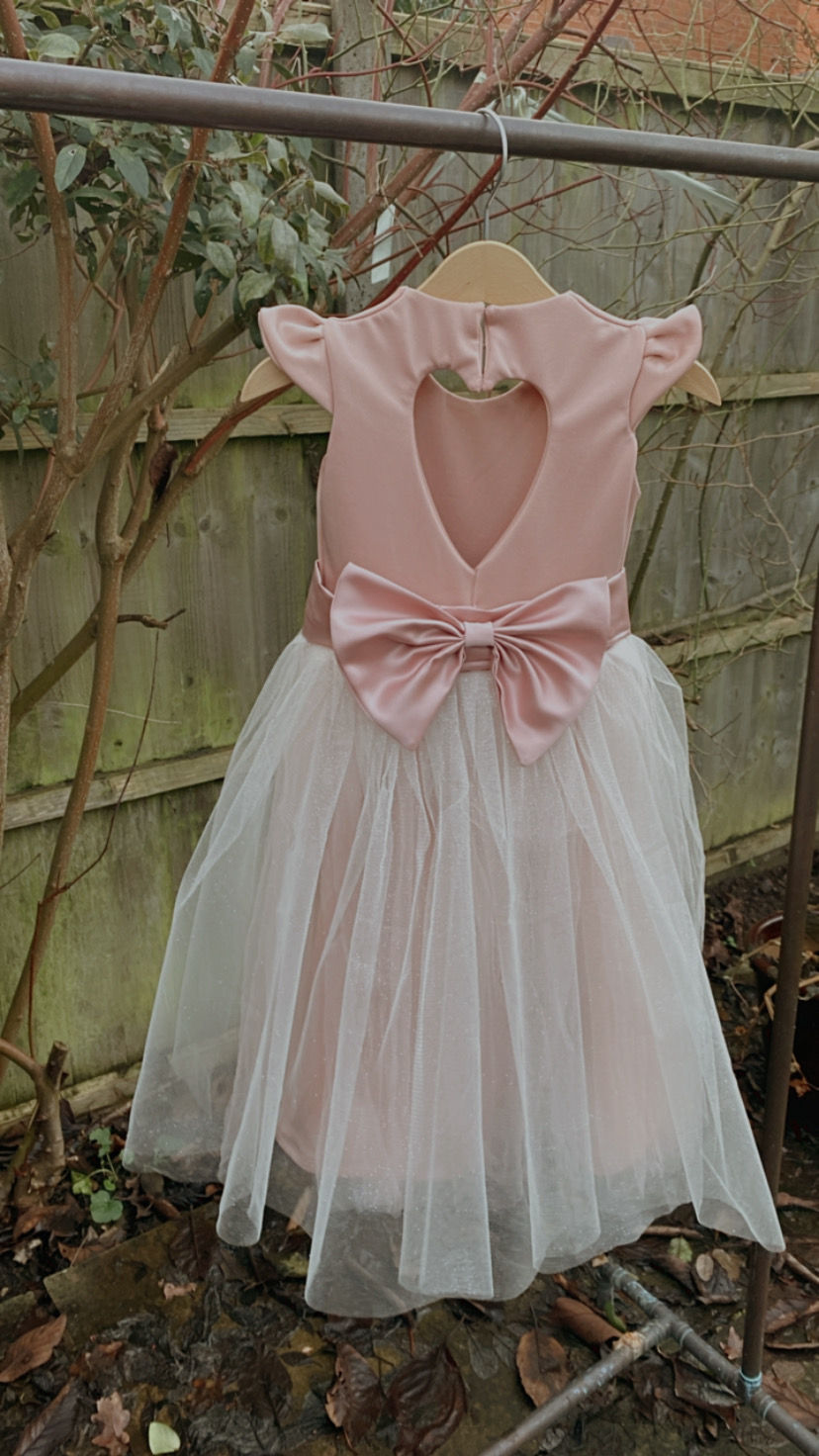 Thumbnail: A handmade small frill sleeve blush pink tutu dress with a heart cut out back and a large duchess satin bow sash. It features a sparkly tulle skirt that falls to the ankle the perfect flower girl or birthday dress