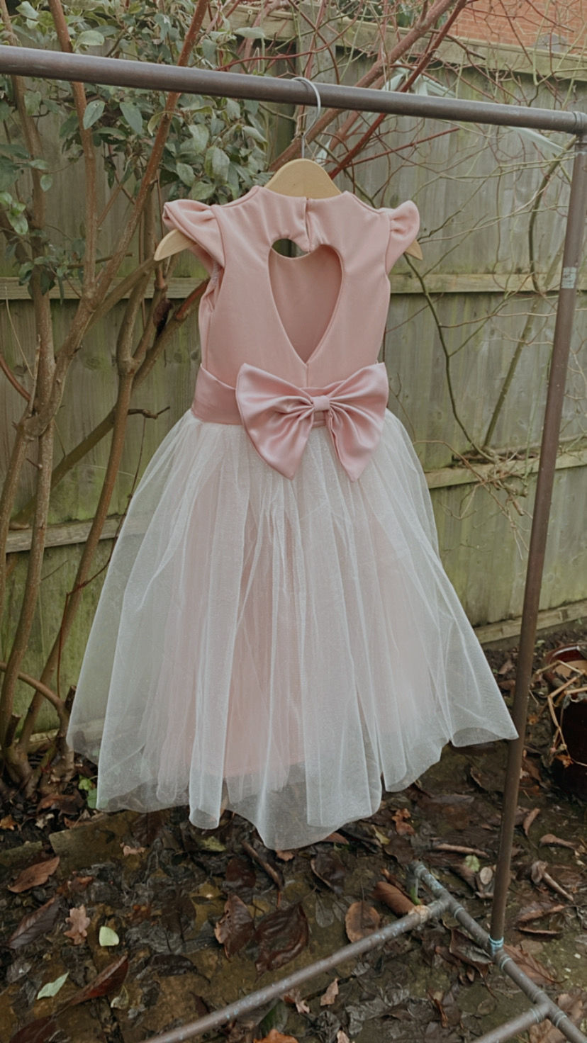 Thumbnail: A handmade small frill sleeve blush pink tutu dress with a heart cut out back and a large duchess satin bow sash. It features a sparkly tulle skirt that falls to the ankle the perfect flower girl or birthday dress