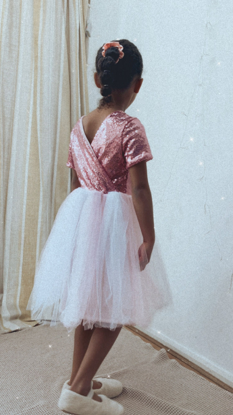 A handmade pink sequin tutu dress with cap sleeves and a crossover back. It features a soft pink tulle skirt that falls just below the knee. The perfect flower girl, birthday dress or Christmas party dress