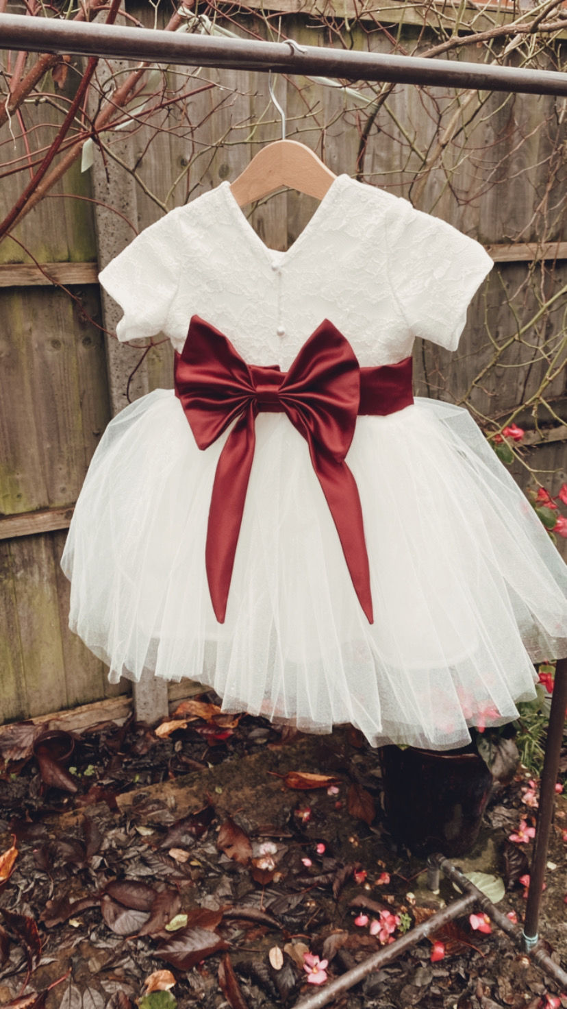 Thumbnail: A handmade cap sleeve lace ivory white tutu dress with a V pearl button back and a large wine duchess satin bow sash. It features a soft ivory white tulle skirt that falls to the knee the perfect flower girl or birthday dress