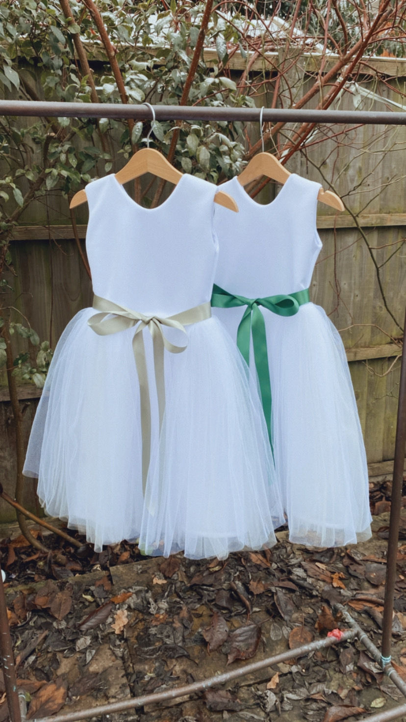 Thumbnail: A handmade sleeveless ivory white tutu dress with a plain back and a soft sage & emerald green ribbon bow sash. It features a soft ivory white tulle skirt that falls to the ankle the perfect flower girl or birthday dress