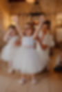 two flower girls wearing an ivory lace top and soft tulle skirt with a large blush bow sash