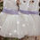 Thumbnail: A handmade ivory white tutu dress with a heart cut out back. It features a sparkly tulle skirt that falls knee length, and has a large lilac duchess satin bow sash. The perfect flower girl, birthday dress or Christmas party dress