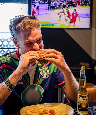 A man enjoying a burger at John Barleycorn’s Taphouse Newmarket with live sports playing on screens in the background, the ultimate sports bar experience in Newmarket Auckland.