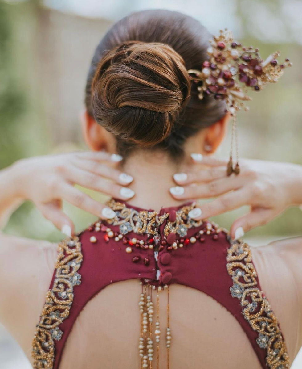 Woman with updo, ornate hair accessory, and embroidered maroon dress
