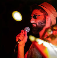 Andrew Meraldson wearing a hat and sunglasses during a live stage performance.