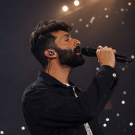 Andrew Meraldson singing into a handheld microphone during a live stage performance.