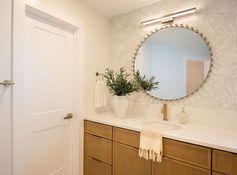 Jacksonville Beach bathroom renovation with light wood vanity, white quartz countertop, round mirror, brass faucet, terrazzo floors and patterned wallpaper.