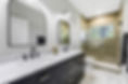 After renovation, the Jacksonville Golf & Country Club primary bathroom designed by Zen Reno & Design with a dark double vanity, marble countertops, arched mirrors, black fixtures, frameless shower glass, and marble look tile.