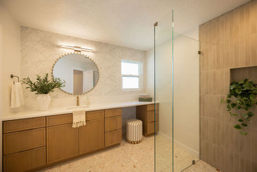 Jacksonville Beach bathroom renovation with light wood vanity, white quartz countertop, round mirror, brass faucet, terrazzo floors and patterned wallpaper.