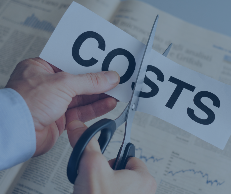 Hands cut paper labeled COSTS with scissors over financial newspaper charts, symbolizing cost cutting.