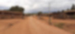 A red dirt road passing trough a number of make-shift wooden houses