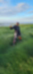 A colored man in motorbike wear in a grass area with lake in the background