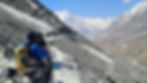 Motorcyclists in helmets ride through a snowy mountain pass. Rugged terrain surrounds them under a clear blue sky.
